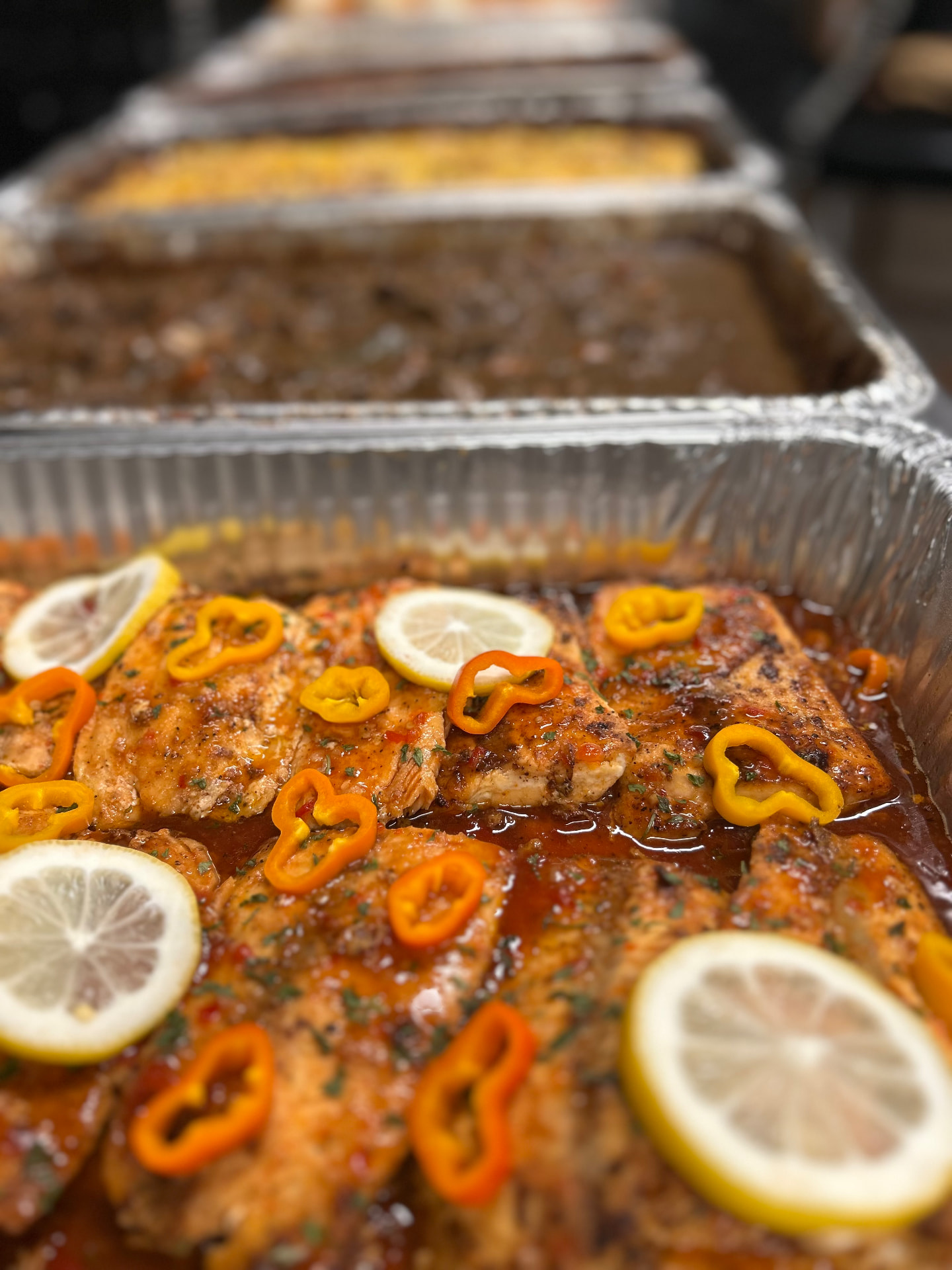 Sweet chili salmon garnished with lemon and sweet peppers in a catering pan