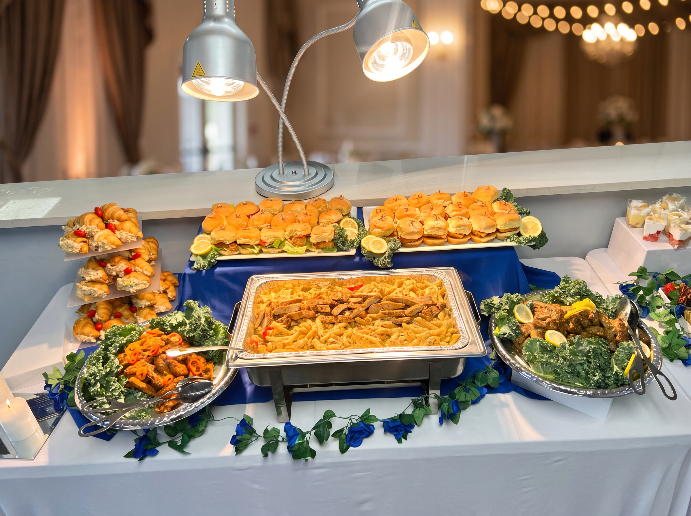Buffet display with sliders, croissant sandwiches, pasta, and desserts