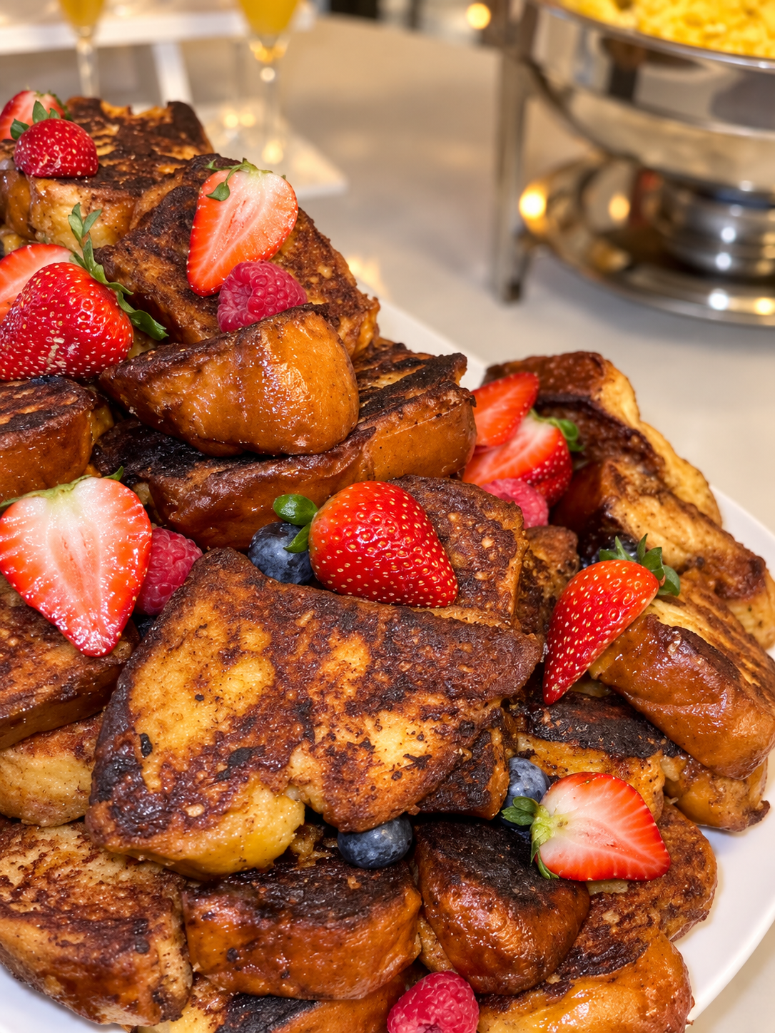 Platter of golden brioche French toast topped with strawberries, raspberries, and blueberries