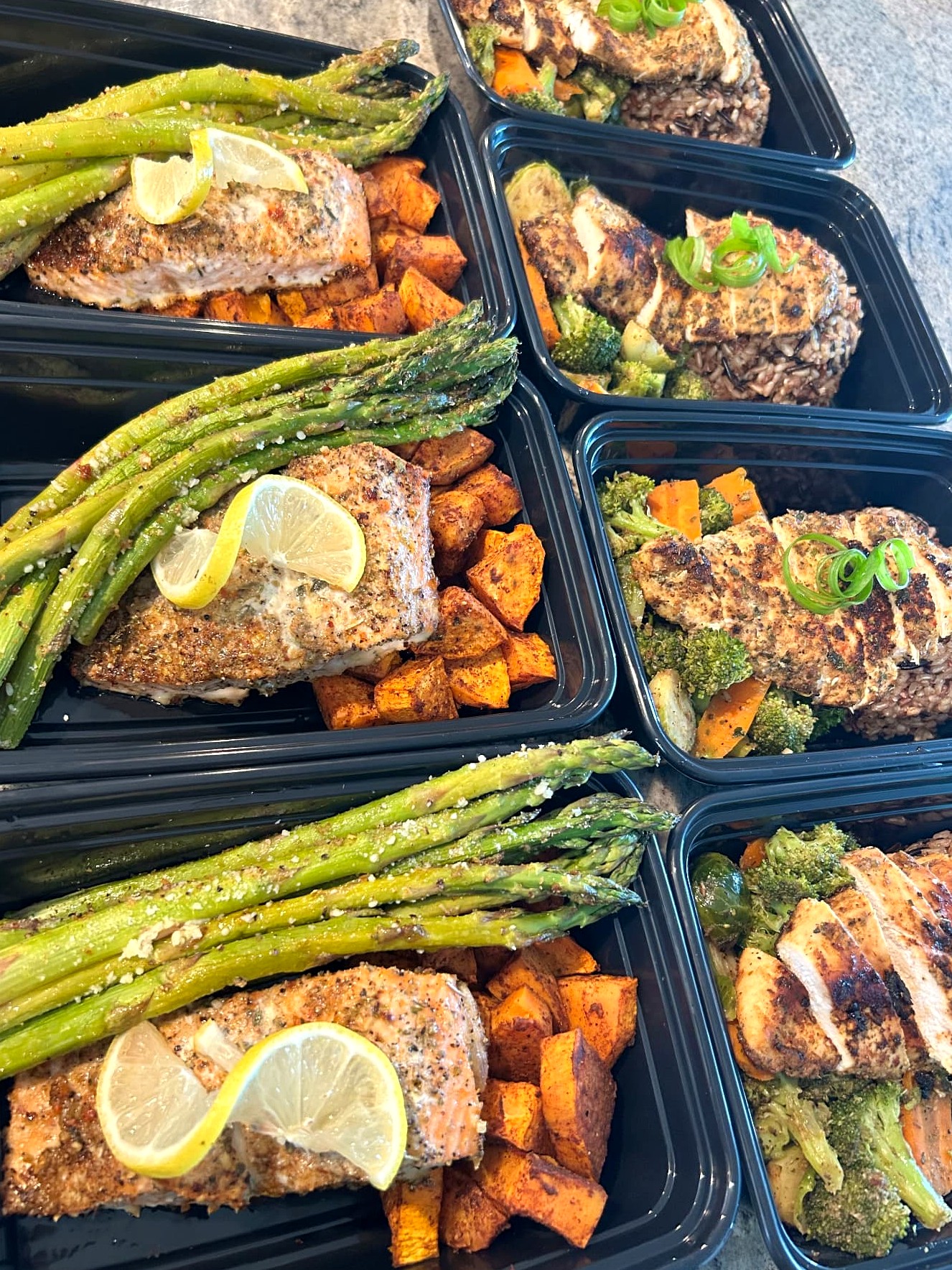 Meal prep containers with seasoned salmon, asparagus, sweet potatoes, herb chicken, wild rice, and vegetables