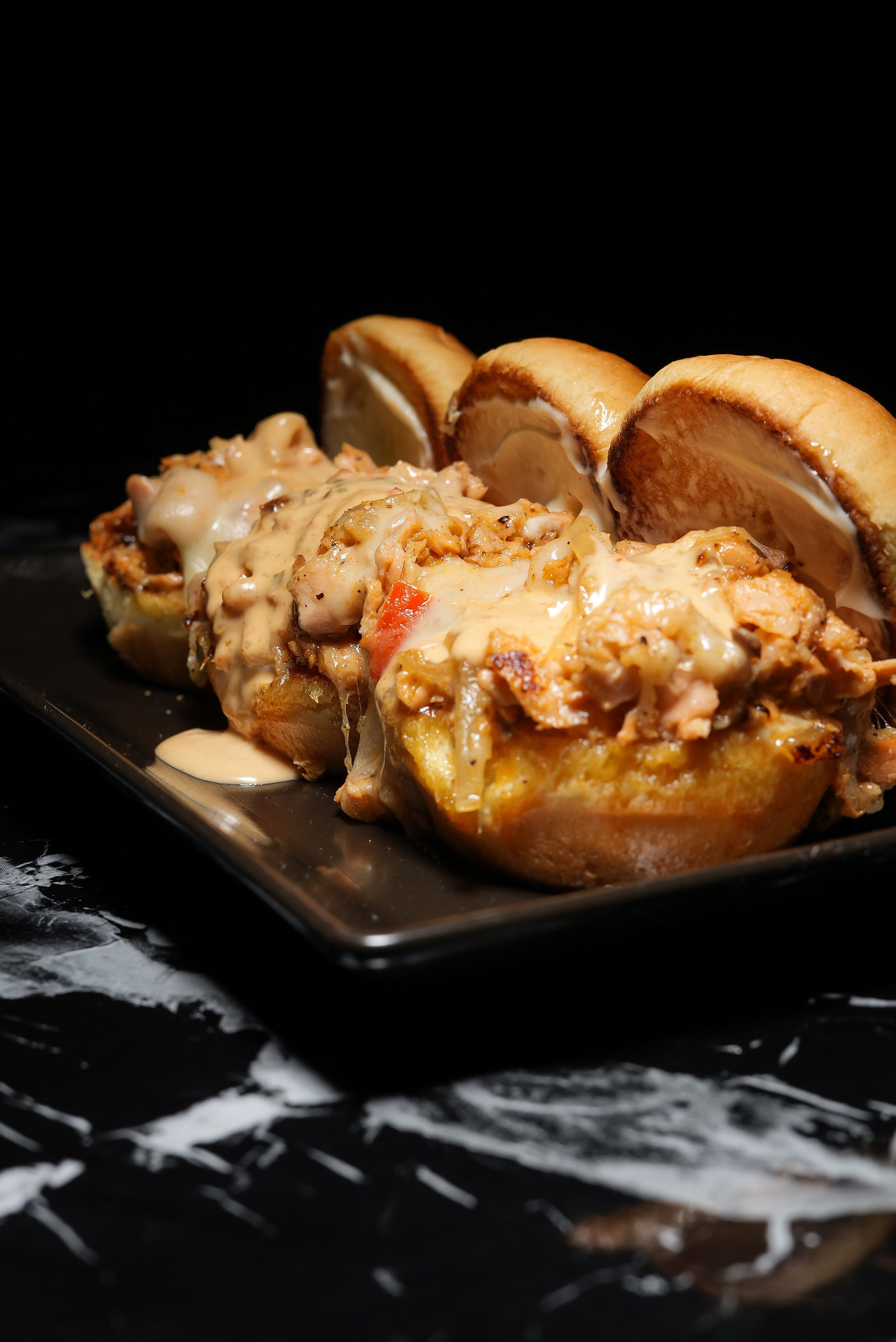 Salmon sliders with melted cheese and sauce on a dark serving platter